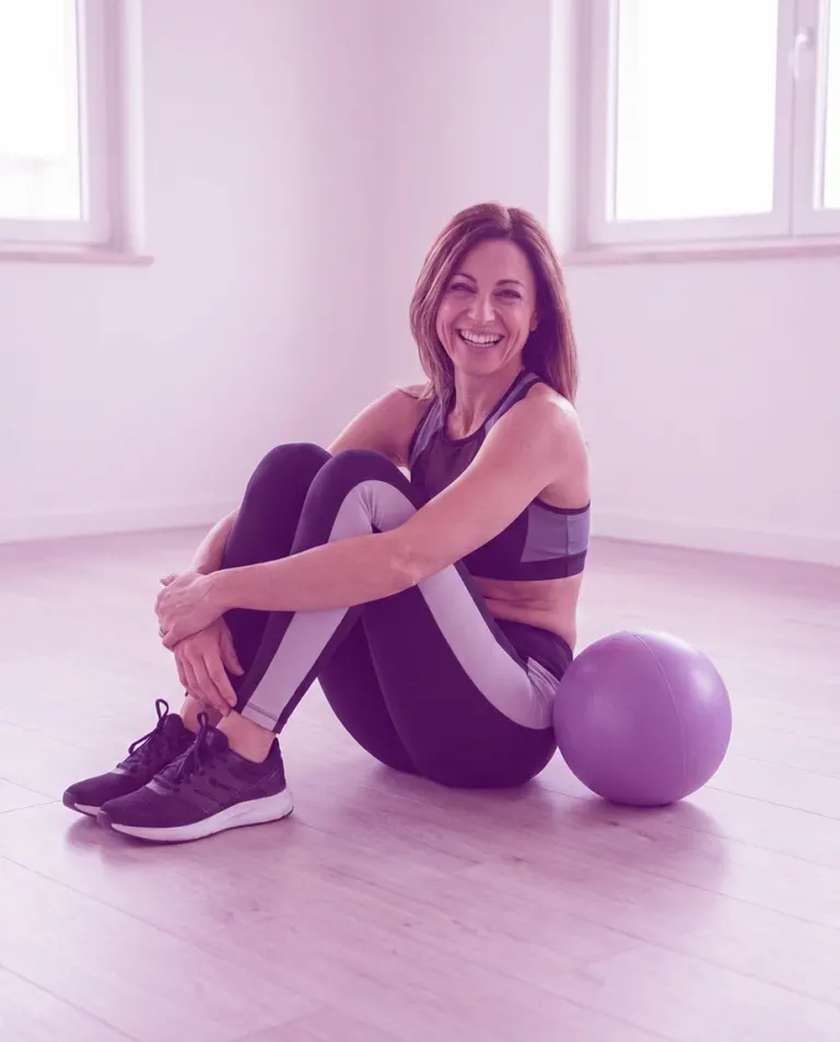 Donna seduta sul tappetino accanto alla fitball lilla