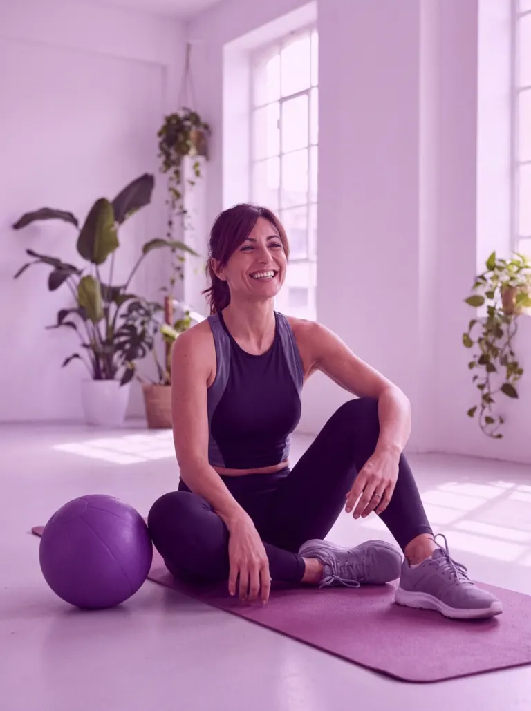 Donna sorridente sul tappetino lilla con la fitball